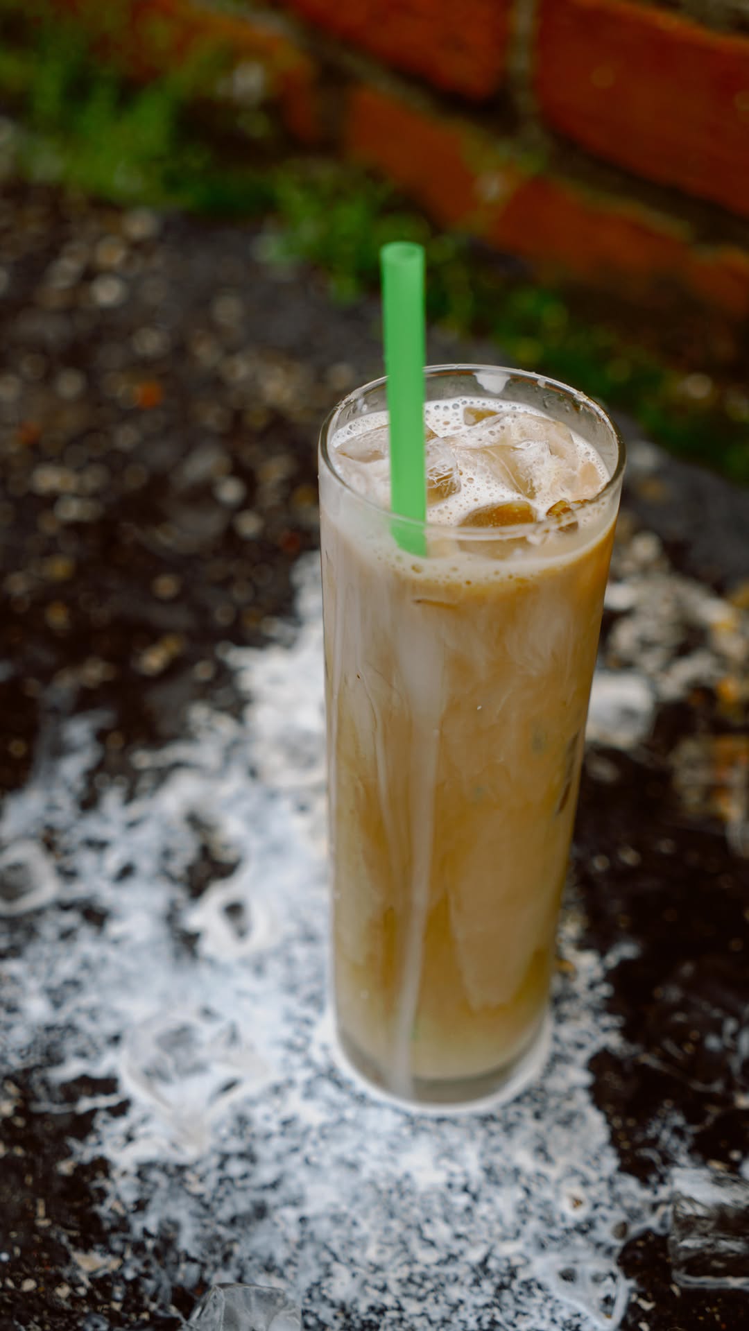 Close-up of a tall iced coffee with cream swirls and a green straw, served at Erie + Vine in downtown Willoughby, Ohio, resting on a moody patio surface with melting ice.